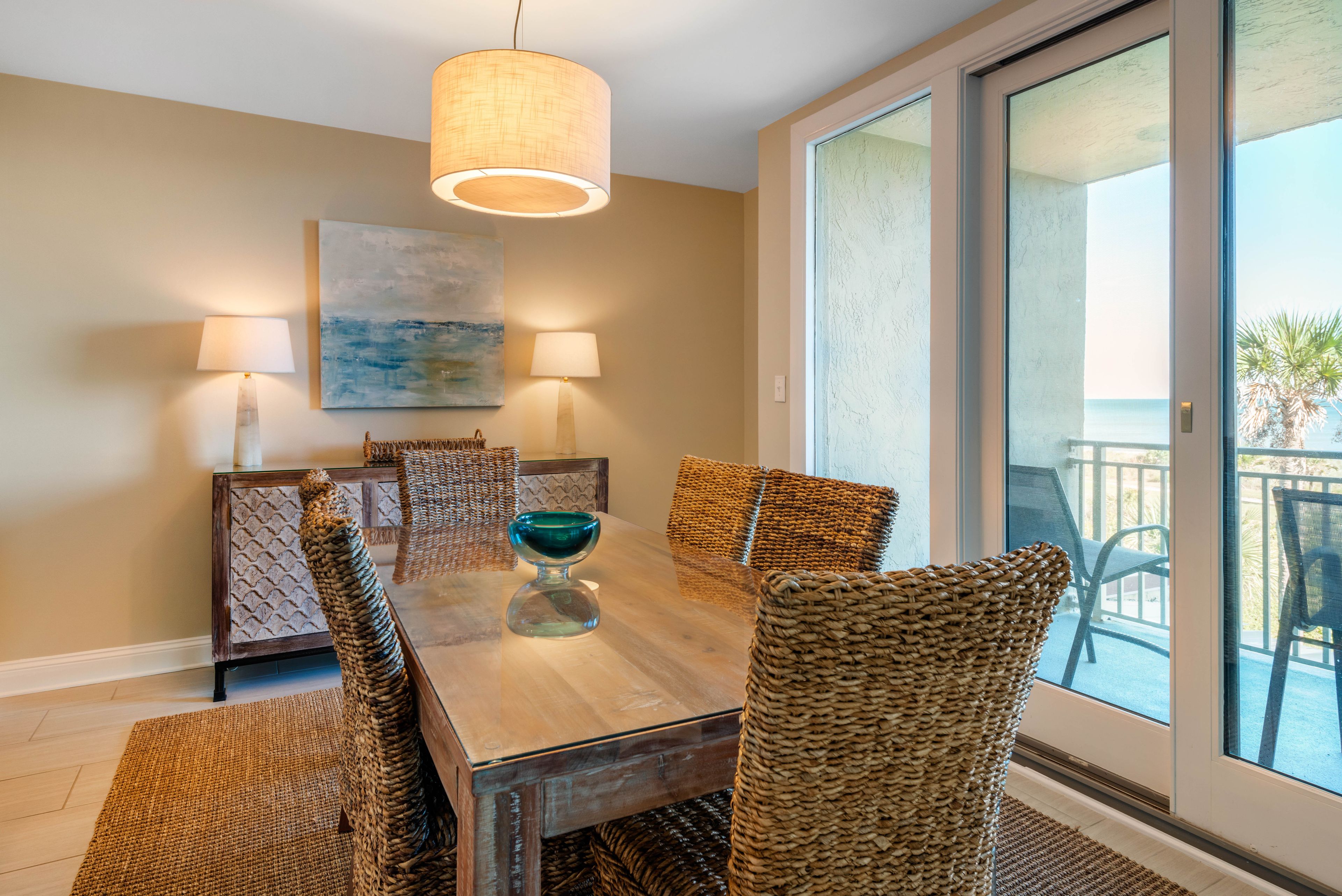 A dining area with a wooden table, woven chairs, and two wall-mounted lamps.