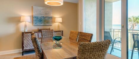 A dining area with a wooden table, woven chairs, and two wall-mounted lamps.