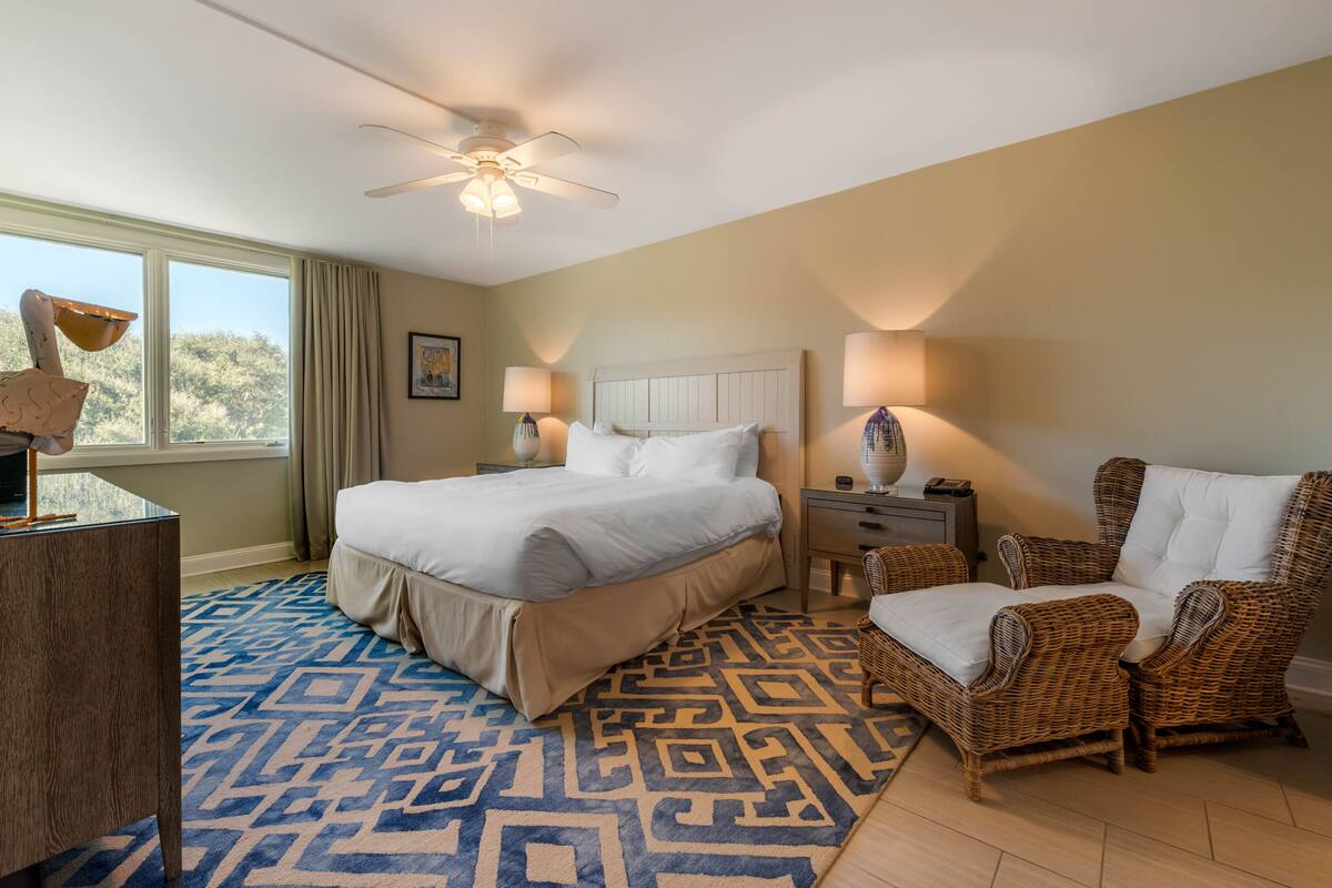 A hotel room with a large bed, two nightstands, a chair, a desk, and a ceiling fan.