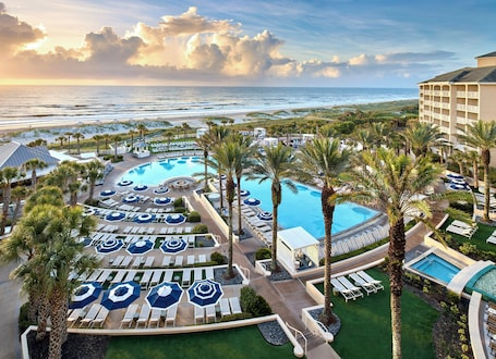 A resort with a large pool, sun loungers, palm trees, and a view of the ocean.
