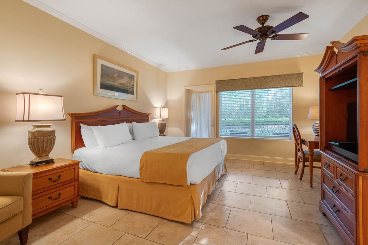 A hotel room with a large bed, a ceiling fan, a desk with a chair, and a television.