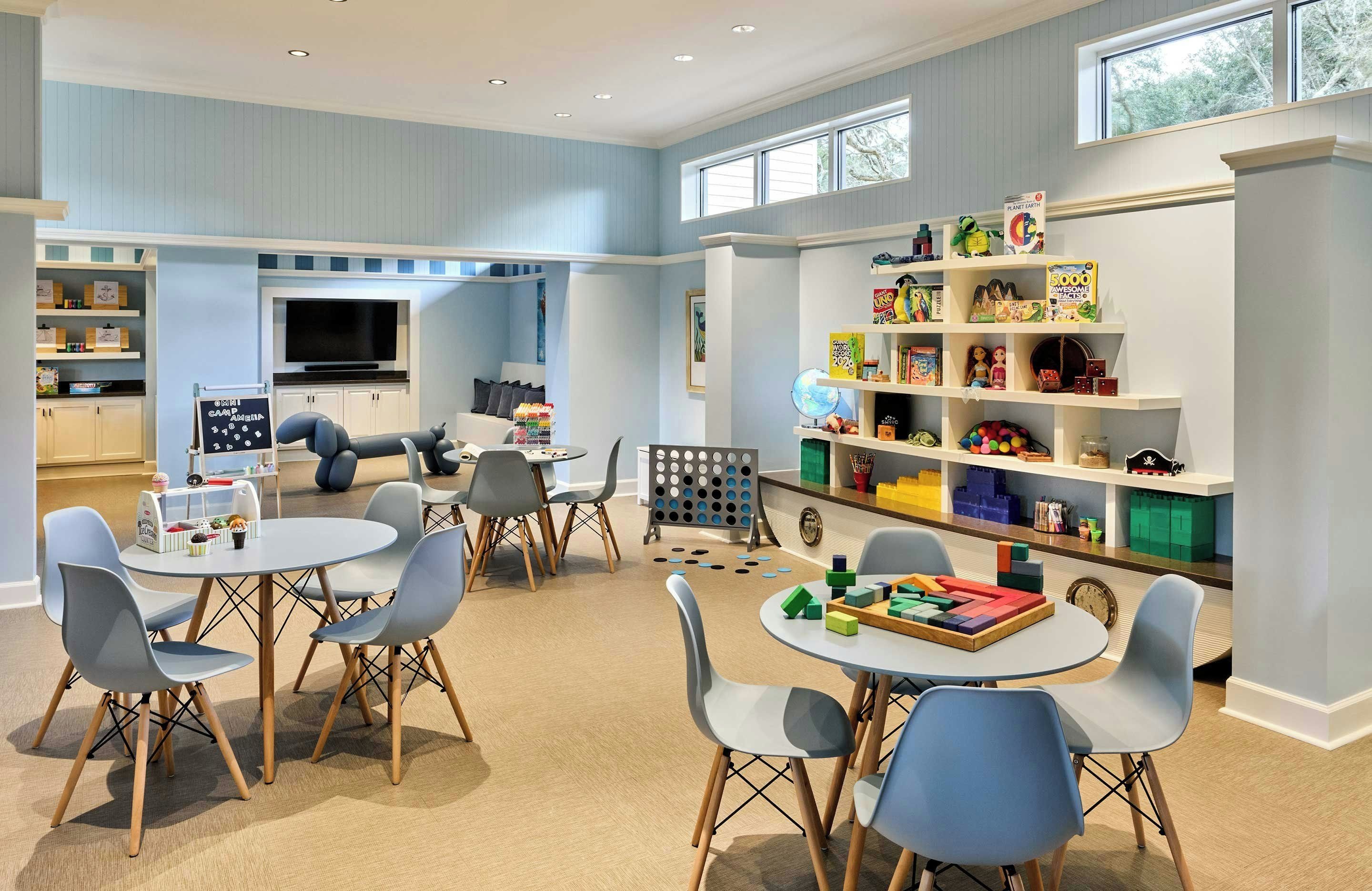 A children's playroom with a TV, shelves with toys, and a table with chairs.
