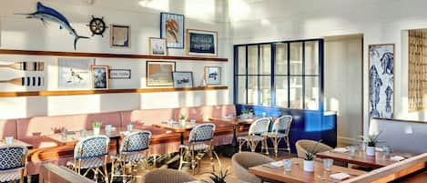 A restaurant with wooden tables and chairs, a large window, and wall art including a fish and a ship's wheel.