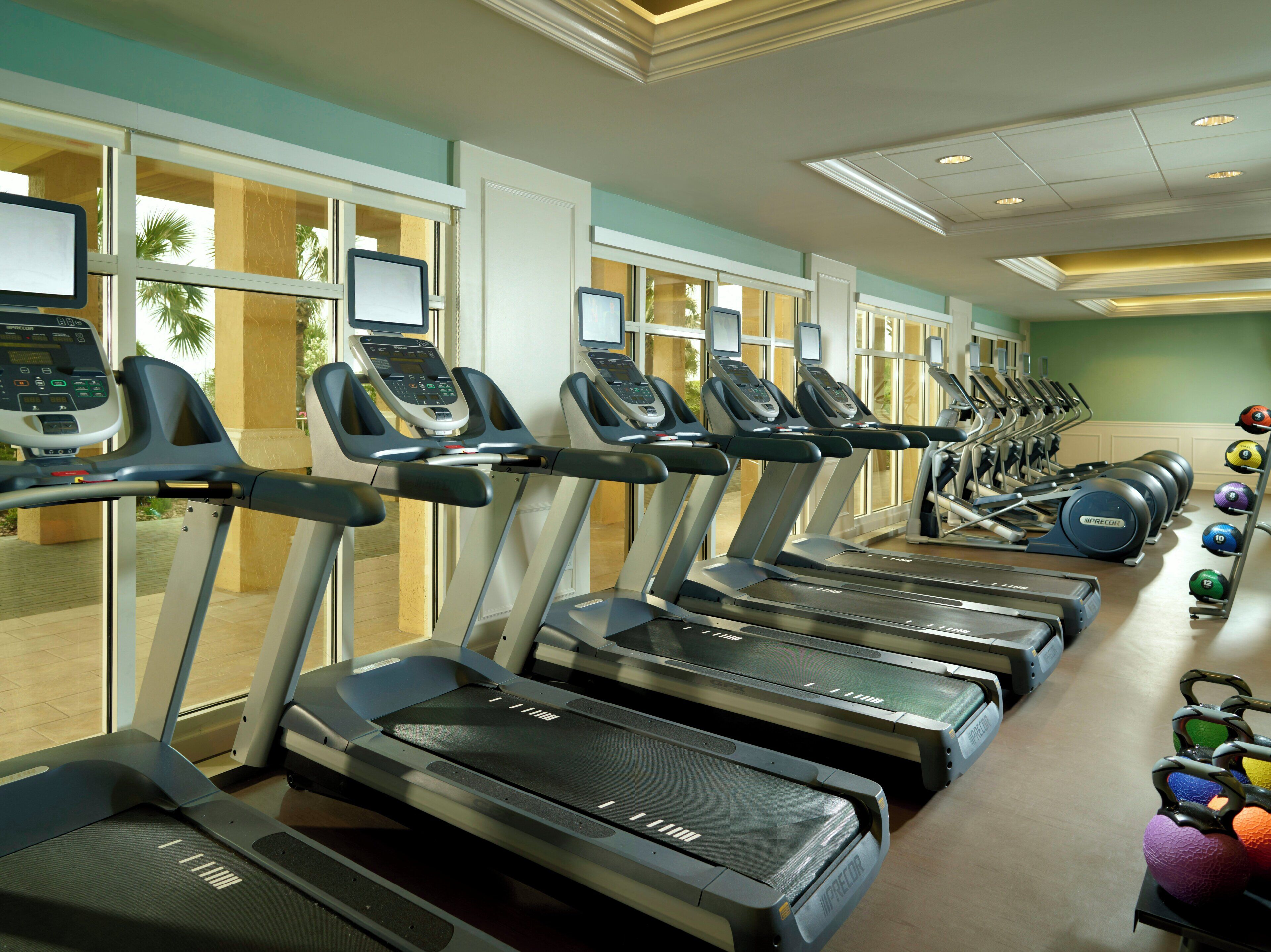 A gym with multiple treadmills, exercise balls, and a row of windows.
