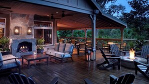 A covered outdoor patio with a stone fireplace, seating, and a fire pit.
