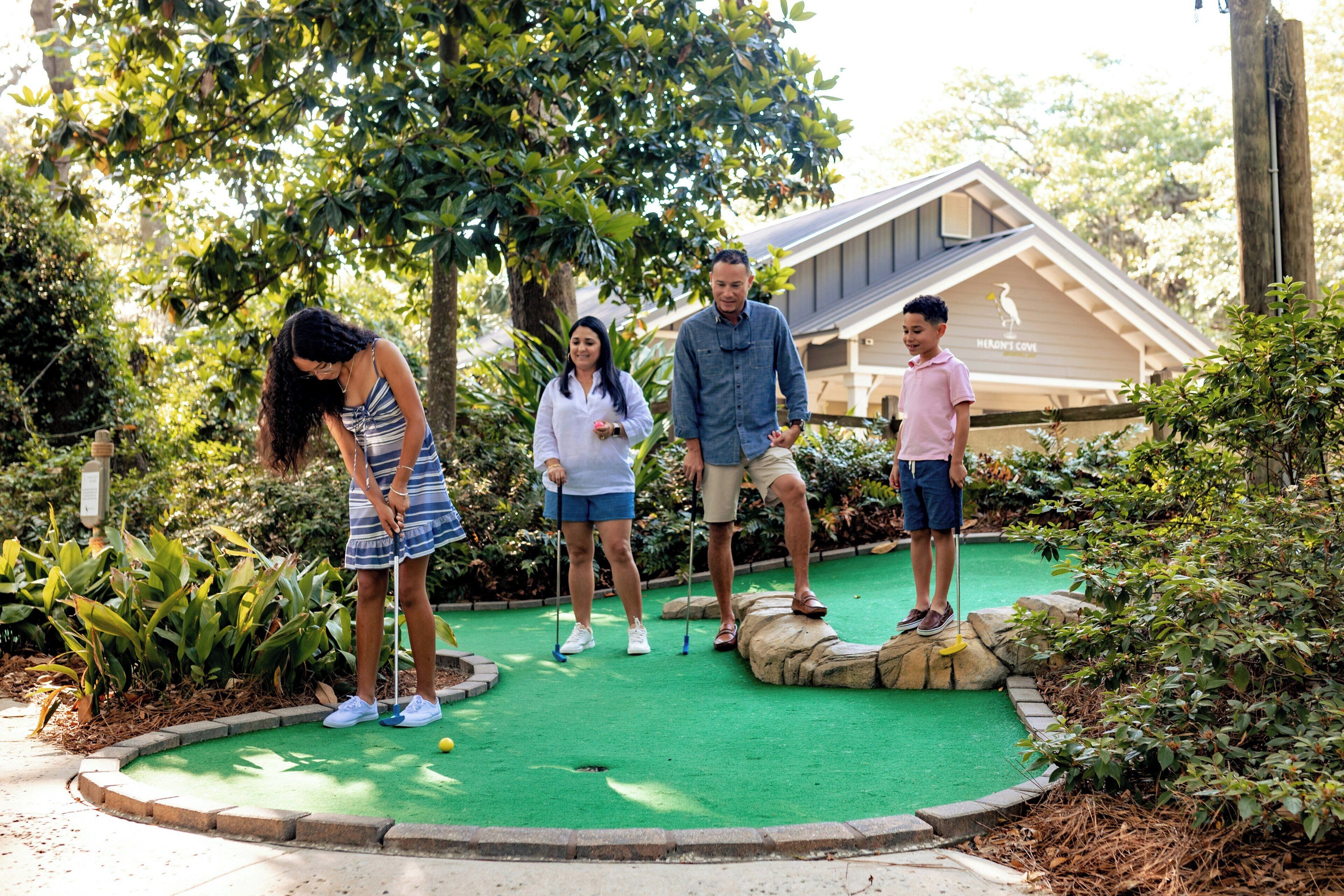 Un groupe de personnes jouant au mini-golf dans un jardin, avec une maison en arrière-plan.