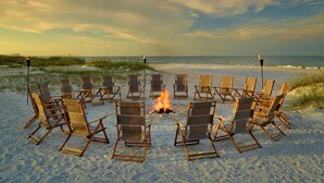 A beach scene with a fire in the center surrounded by beach chairs.