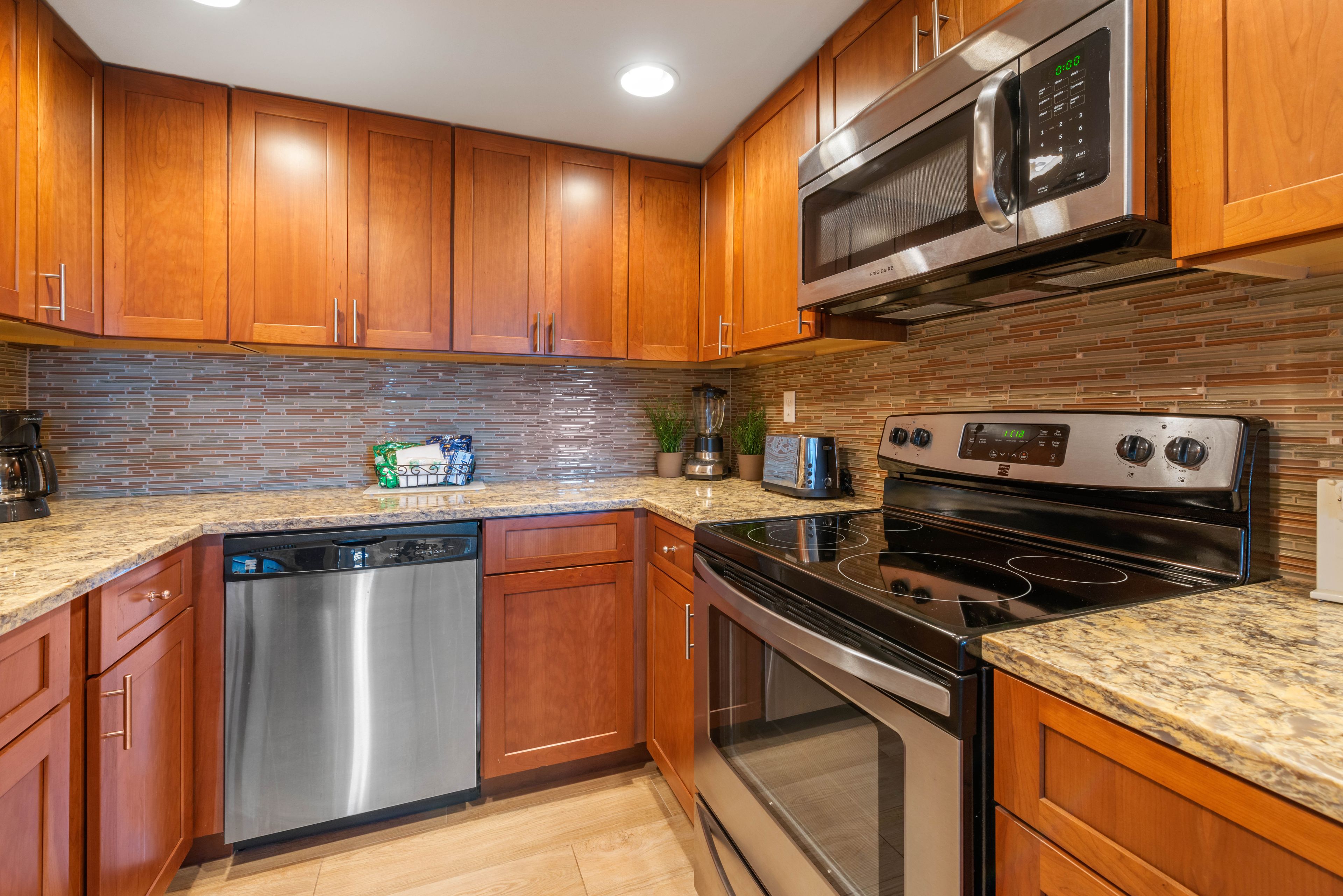 A kitchen with wooden cabinets, a stainless steel dishwasher, a microwave, a toaster, and a stove.