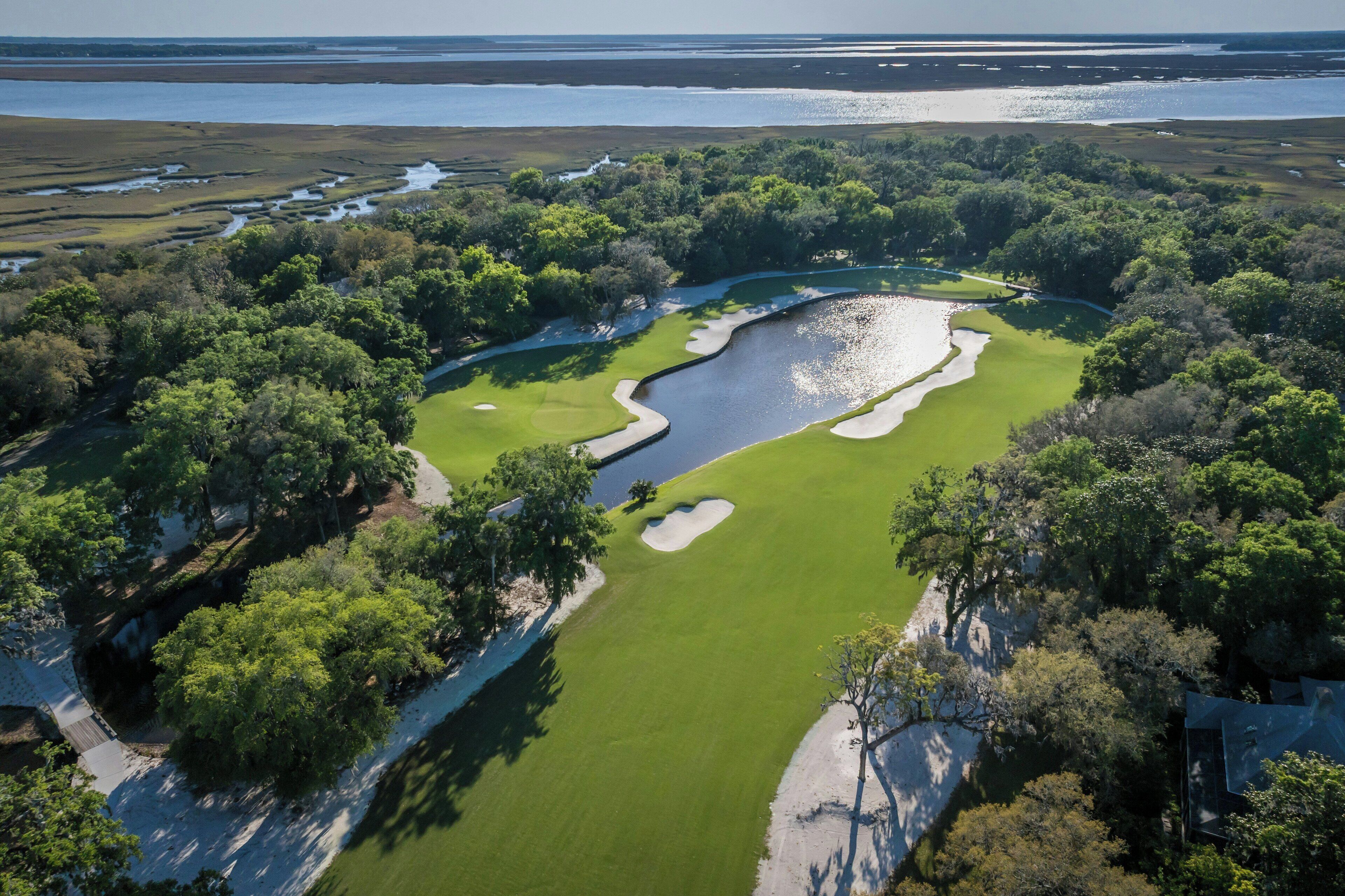 An aerial view of a golf course with sand bunkers, water hazards, and dense trees.