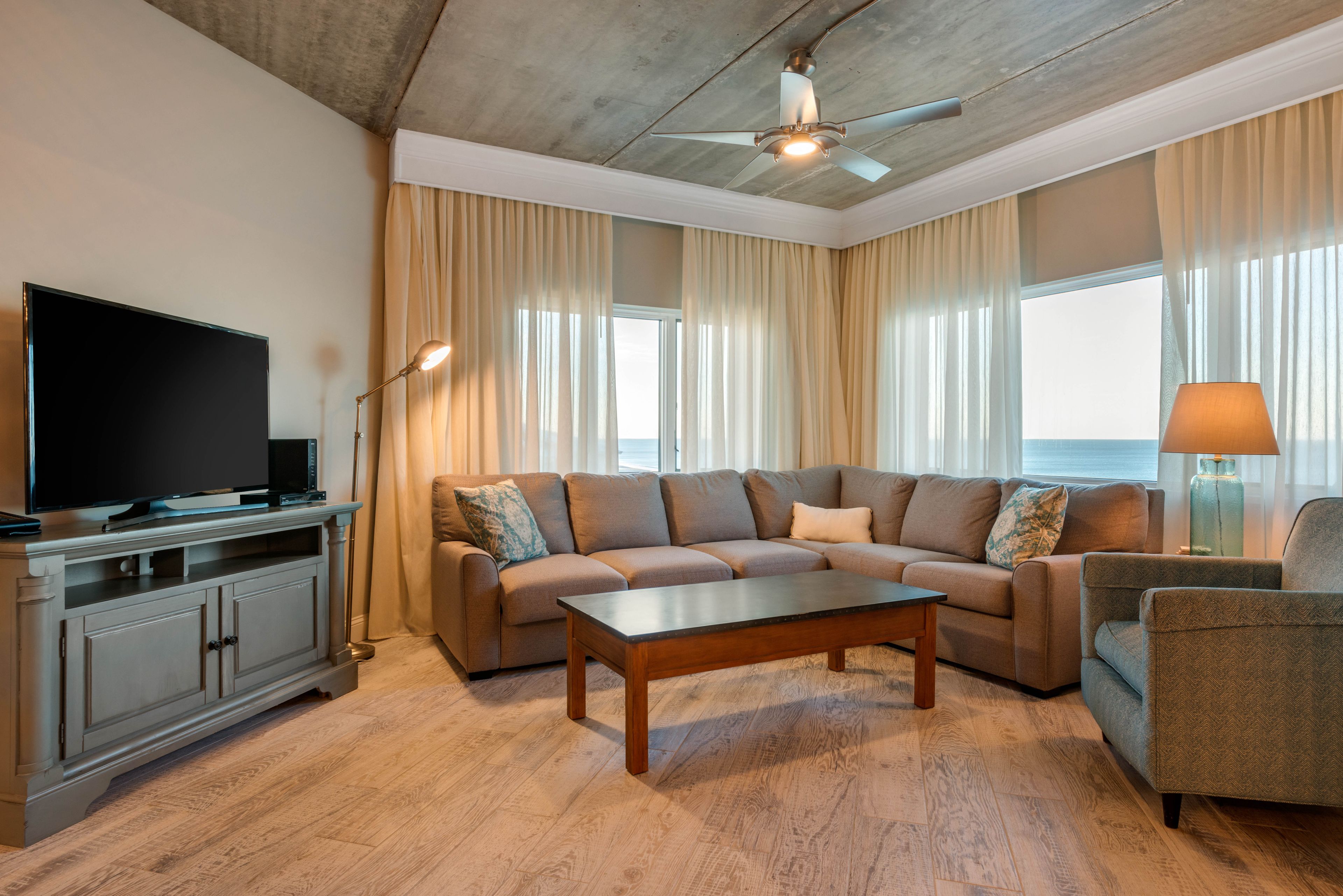 A modern living room with a sectional sofa, a flat-screen TV, a coffee table, and a ceiling fan.