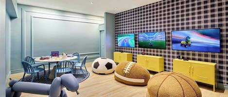 A modern children's play area with a round table, chairs, and large bean bags shaped like sports balls.