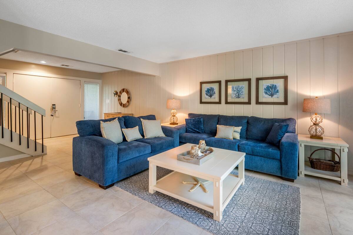 A living room with two blue sofas, a white coffee table, and a patterned rug.