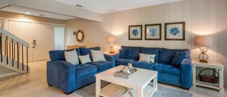 A living room with two blue sofas, a white coffee table, and a patterned rug.
