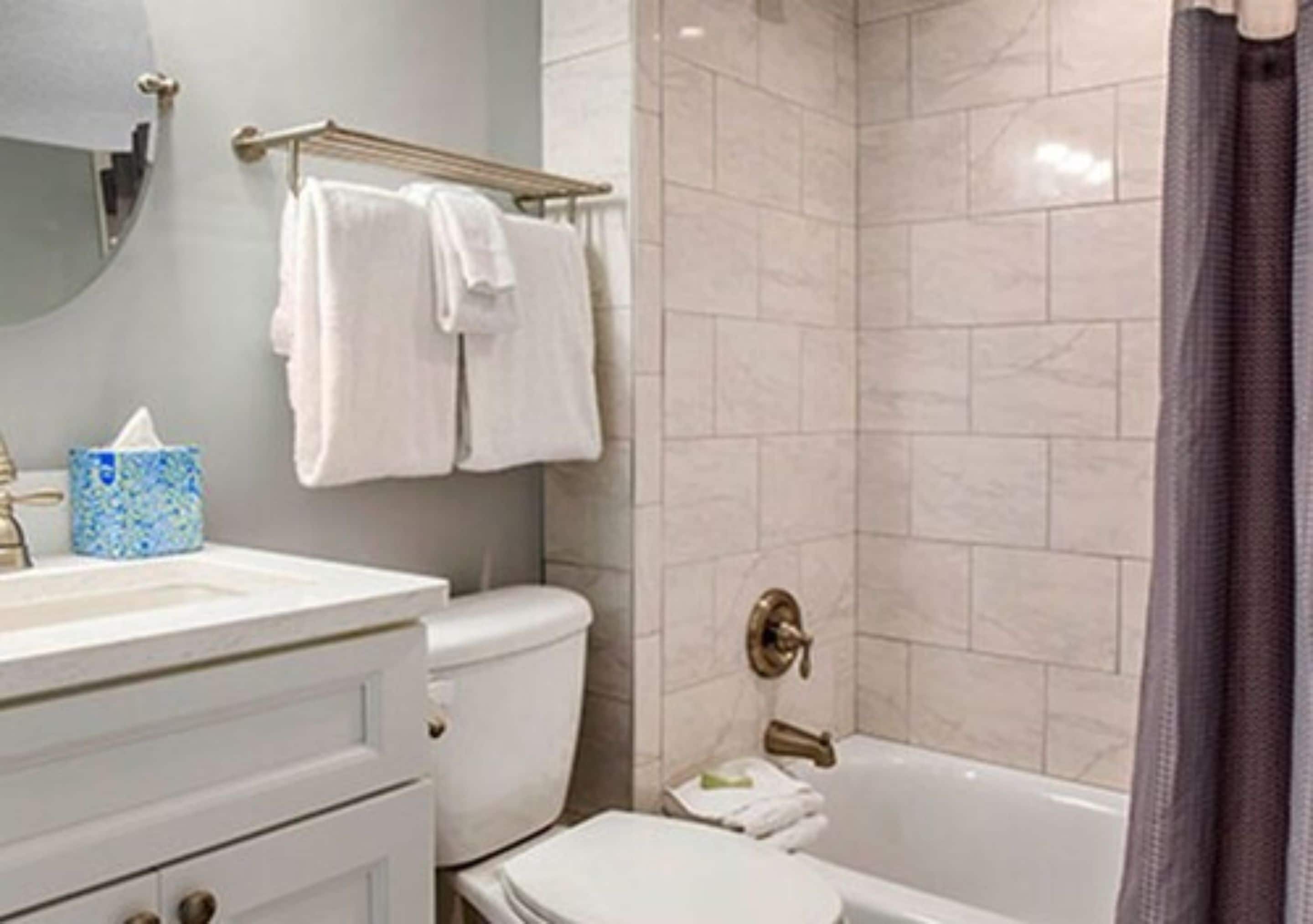 A bathroom with a toilet, sink, and bathtub. There are towels hanging on a rack and a shower curtain.