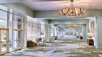A spacious hotel lobby with large windows, a patterned carpet, and a chandelier.