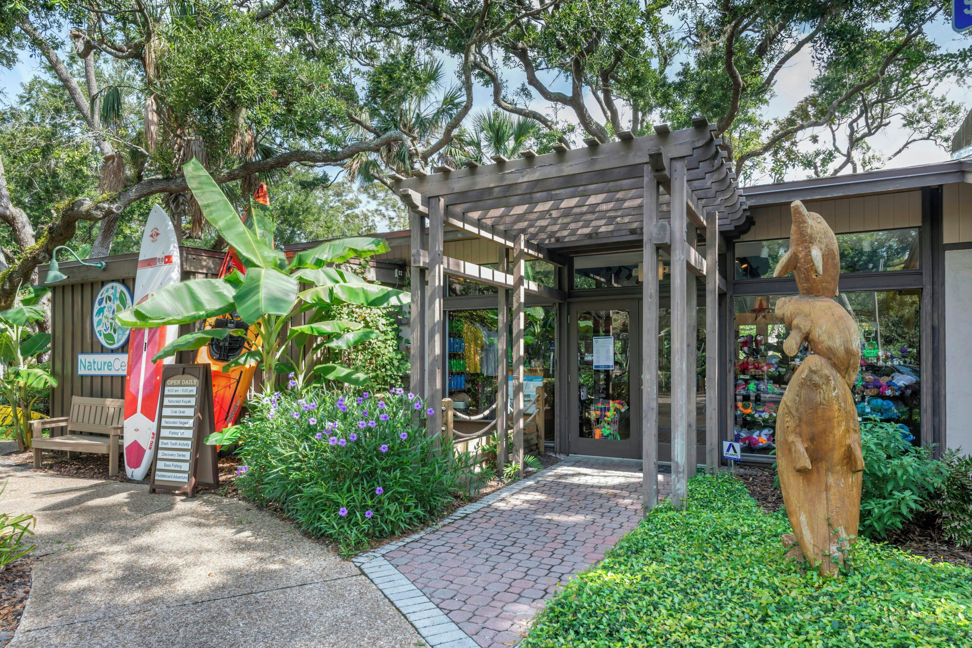 A garden entrance with a wooden bench, a surfboard, and a statue.
