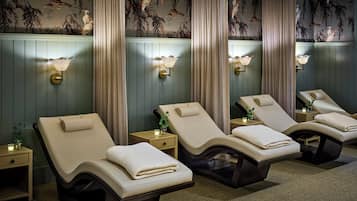 A spa room with four reclining chairs, each with a towel and a small table with a candle.
