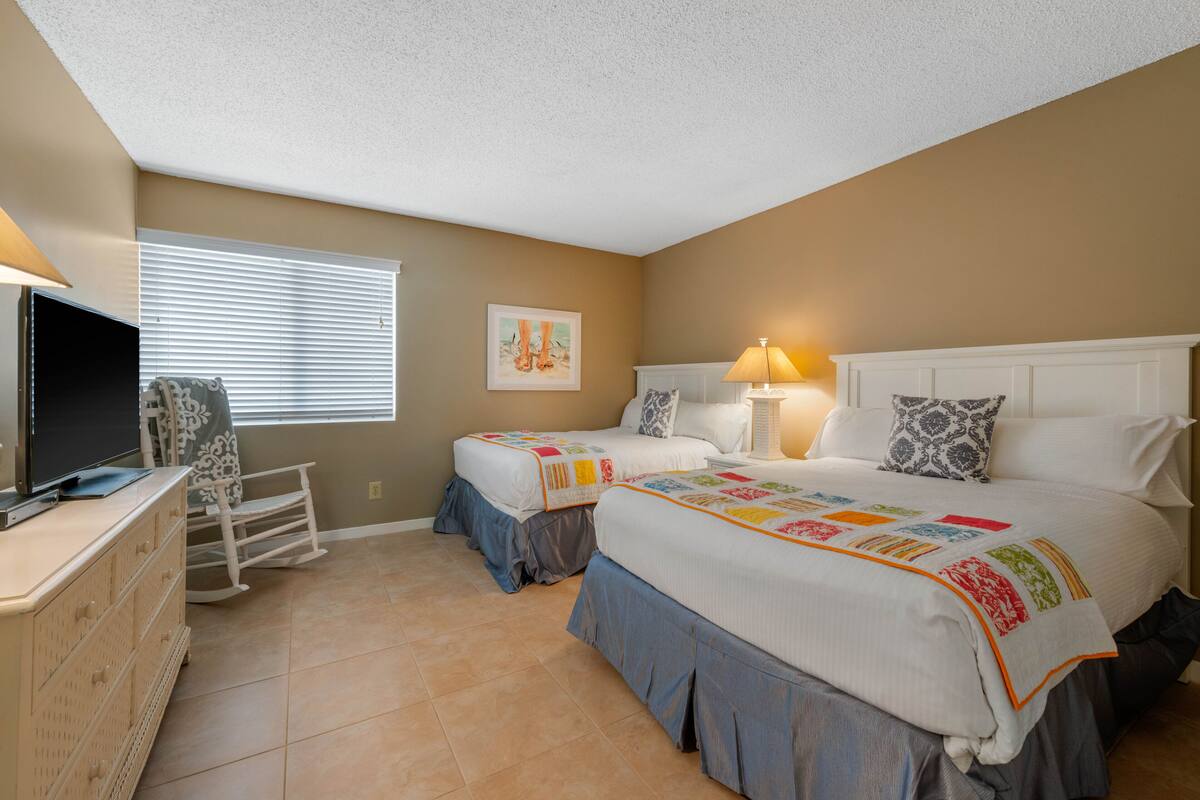 A hotel room with two beds, a TV, a dresser, and a rocking chair.