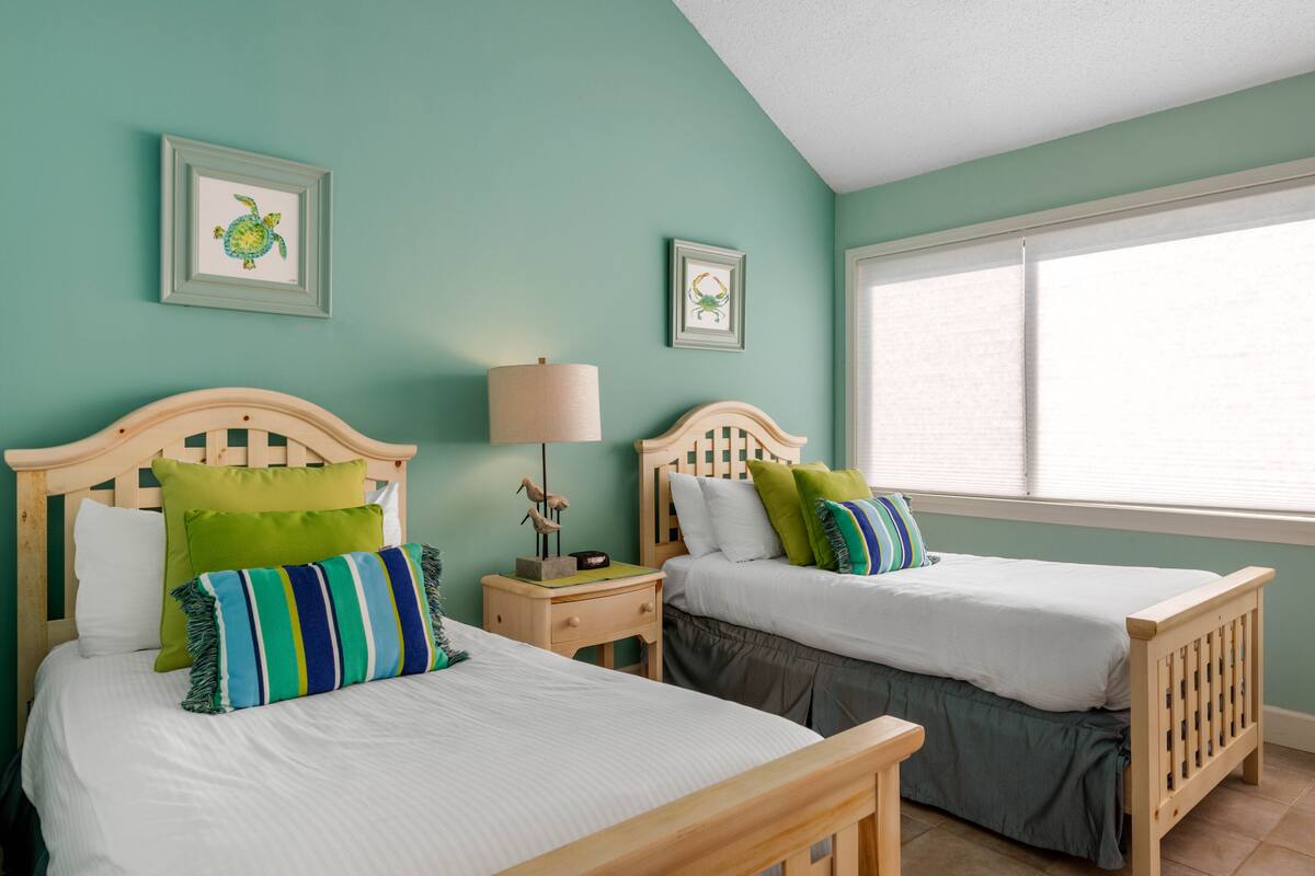 A room with two wooden beds, each with a pillow and a framed picture on the wall.