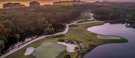 A golf course with bunkers, a water hazard, and a hotel in the background.
