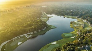 An aerial view of a golf course with water hazards, sand bunkers, and a clubhouse.