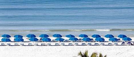 A beach with rows of blue umbrellas and white lounge chairs.