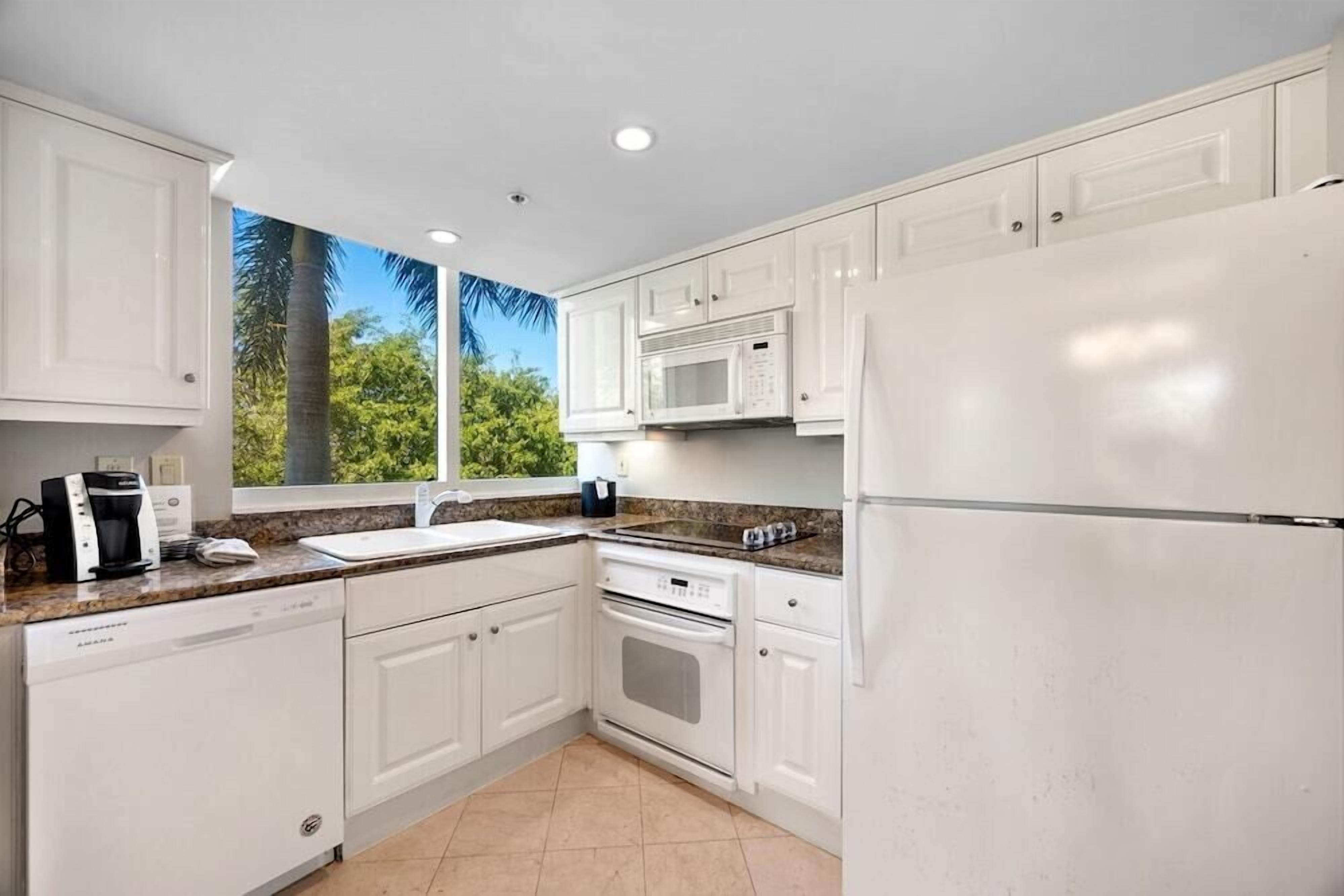 A modern kitchen with white cabinets, a built-in microwave, a refrigerator, and a coffee maker.