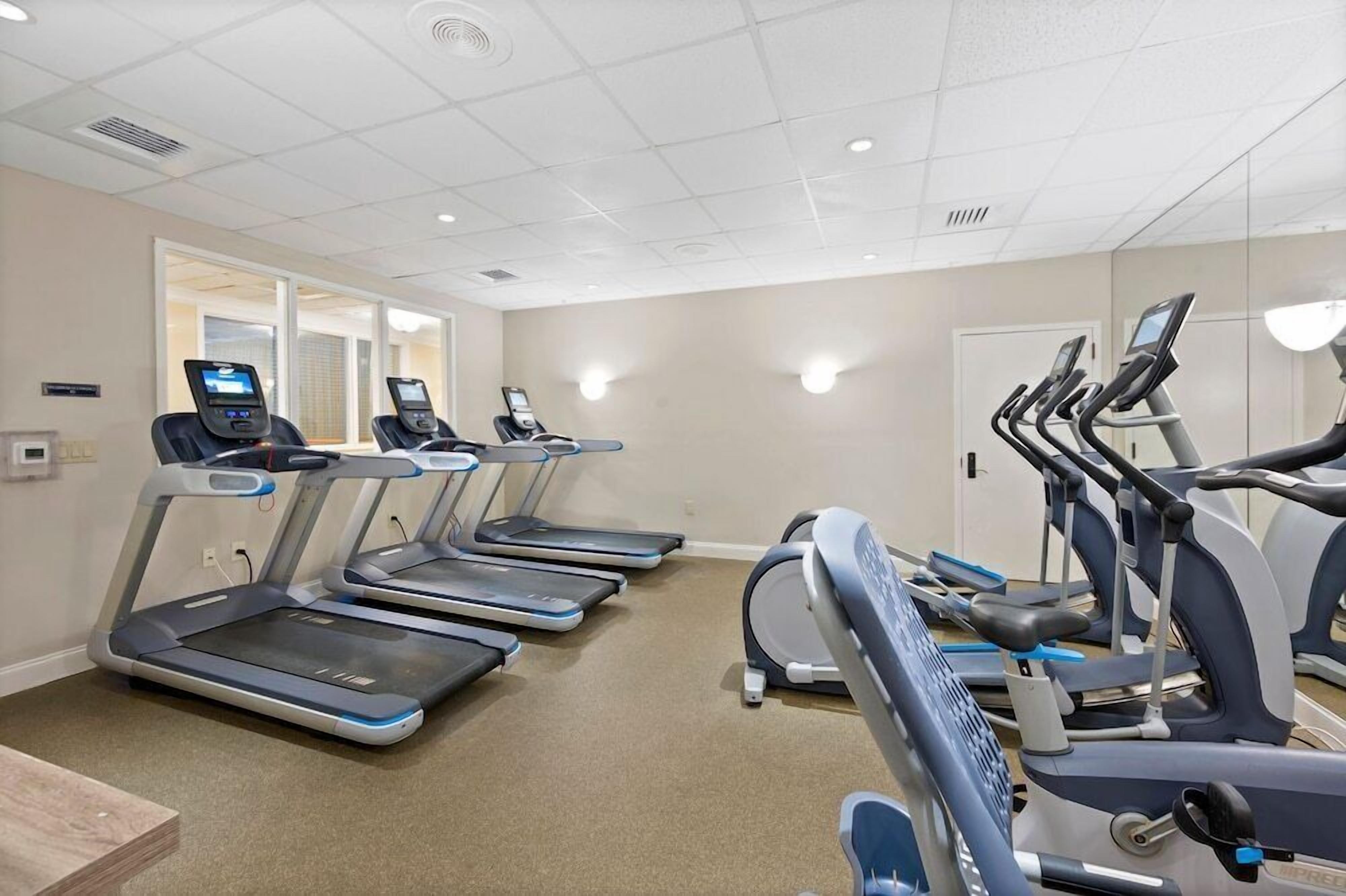 A fitness room with multiple treadmills and elliptical machines, carpeted floor, and a neutral color scheme.