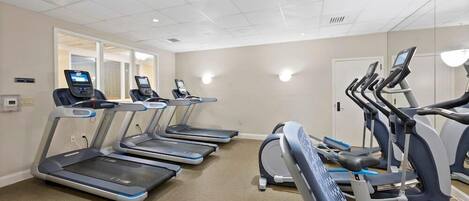 A fitness room with multiple treadmills and elliptical machines, carpeted floor, and a neutral color scheme.