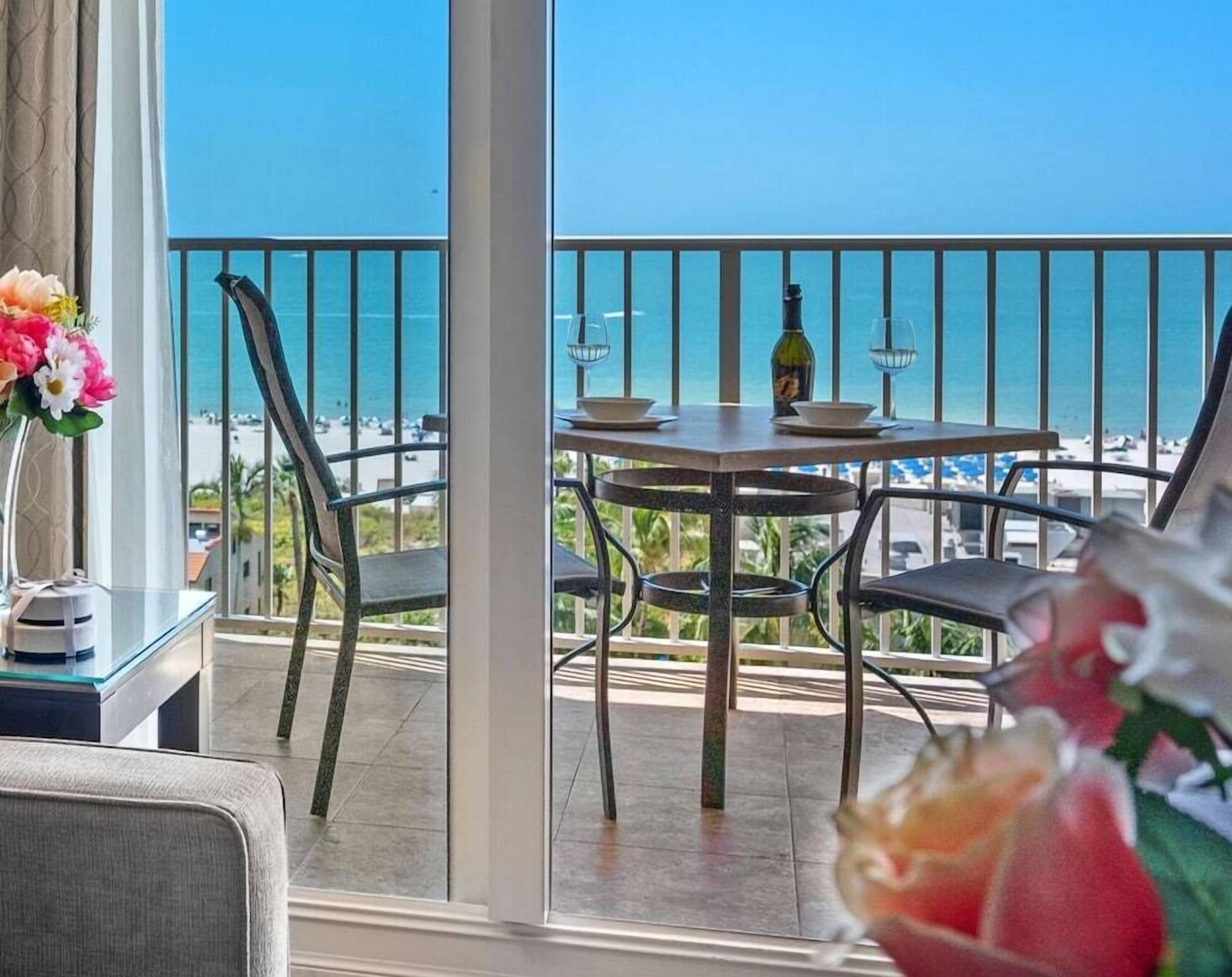 A balcony with a table and chairs, overlooking a beach.
