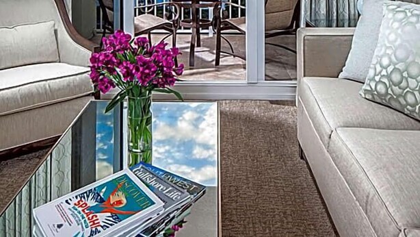 A hotel room with a balcony, a sofa, a coffee table with magazines, and a vase with flowers. - Marco Beach Ocean Resort (Marco Island)