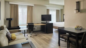 Habitación de hotel con sofá, escritorio, televisor, cama y una mesita.