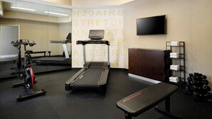 A gym with exercise equipment, a treadmill, a bench, a mirror, and a television on the wall.