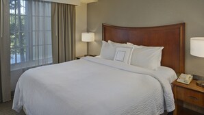 A neatly made bed with white linens, a wooden headboard, a bedside table with a lamp, and a telephone.