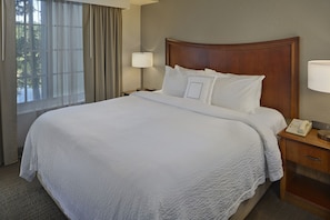 A neatly made bed with white linens, a wooden headboard, a bedside table with a lamp, and a telephone.