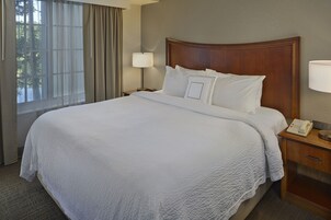 Una cama bien hecha con sábanas blancas, un cabecero de madera, una mesita de noche con una lámpara y un teléfono.