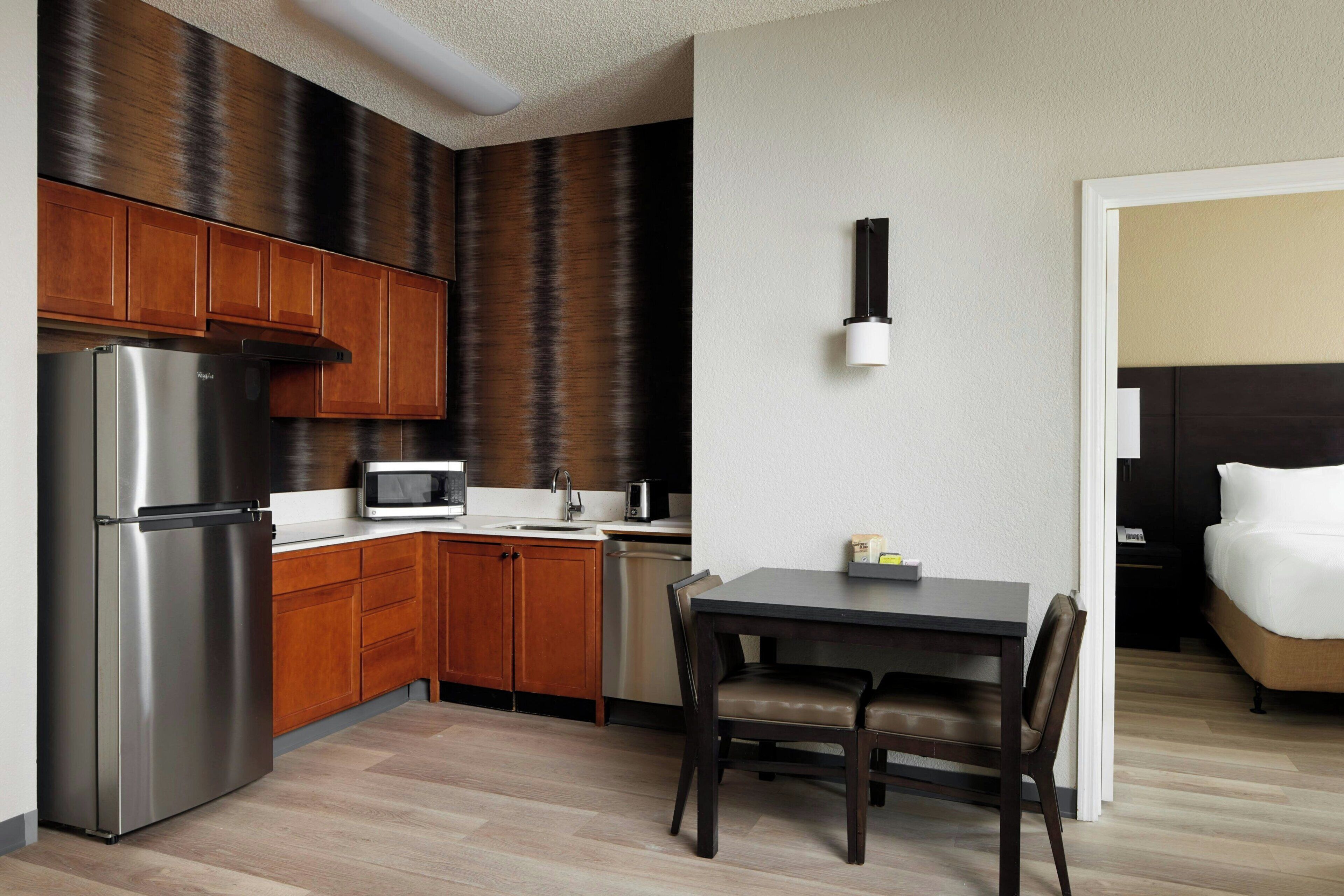 A compact hotel room with a kitchenette, a bed, a dining area, and a bathroom.