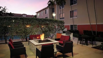 An outdoor seating area with a fire feature, wicker furniture, and a view of a building with a red and beige facade.