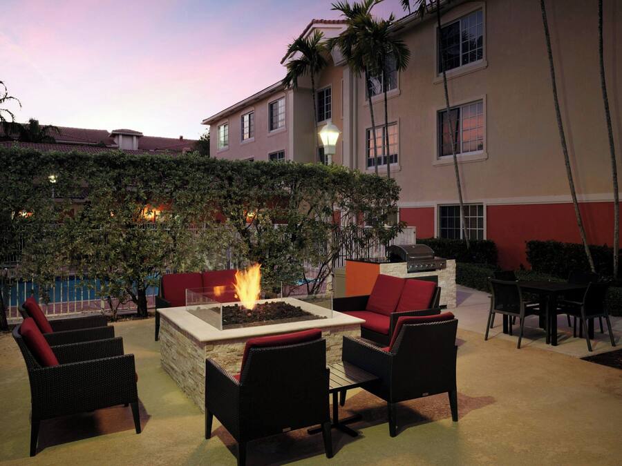 An outdoor seating area with a fire feature, wicker furniture, and a view of a building with a red and beige facade.