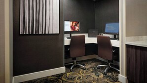 Habitación de hotel con escritorio, dos sillas, una computadora y una televisión mostrando un anuncio.