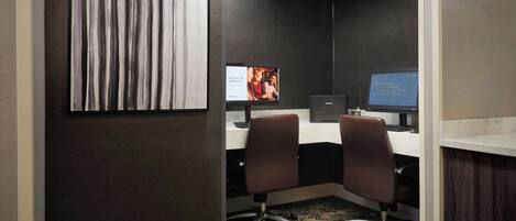 Habitación de hotel con escritorio, dos sillas, una computadora y una televisión mostrando un anuncio.