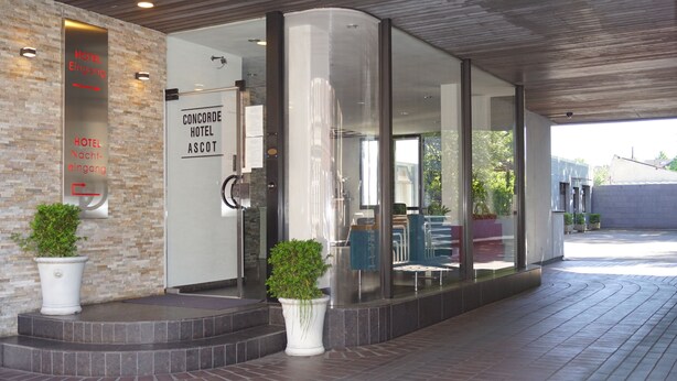 A hotel entrance with glass doors, a sign for the Concorde Hotel Ascot, and potted plants. - Concorde Hotel Ascot (Düsseldorf)