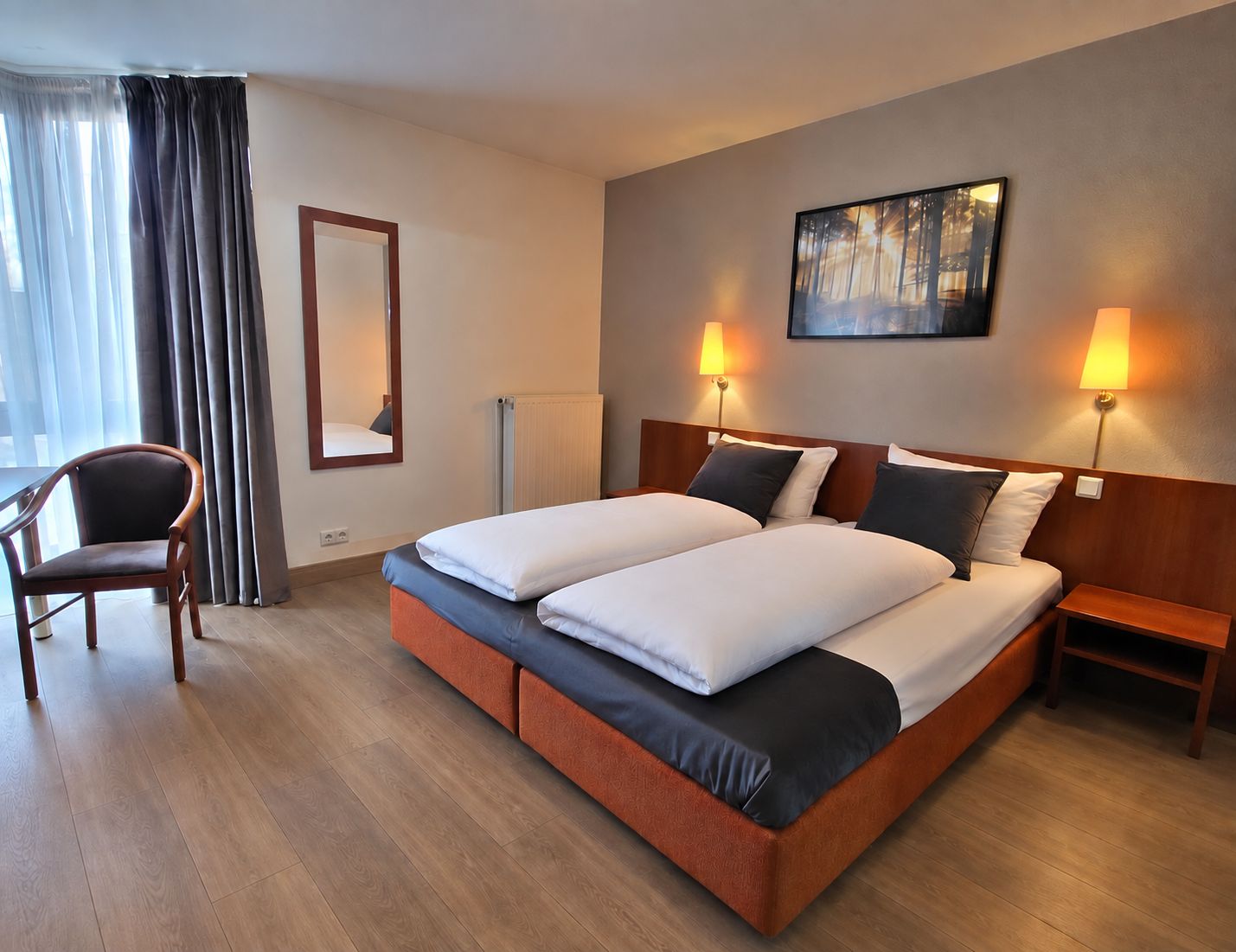 Una habitación de hotel con una cama doble, dos mesitas de noche, una silla, un espejo grande y un cuadro en la pared.