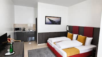 Quarto de hotel com cama, escrivaninha, micro-ondas, pia e um quadro na parede.