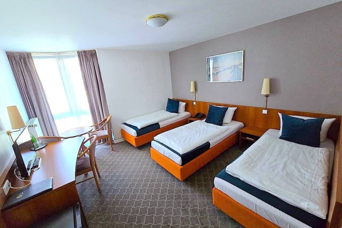 A hotel room with two single beds, a desk with a chair, a lamp, and a painting on the wall.