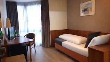 Habitación de hotel con un escritorio de madera, una silla, una cama sofá y un cuadro en la pared.