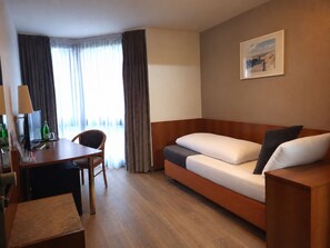 Een hotelkamer met een houten bureau, een stoel, een slaapbank en een schilderij aan de muur.