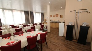 A hotel dining area with multiple tables set for dining, a kitchen in the background, and a reception desk. - Concorde Hotel Ascot (Düsseldorf)