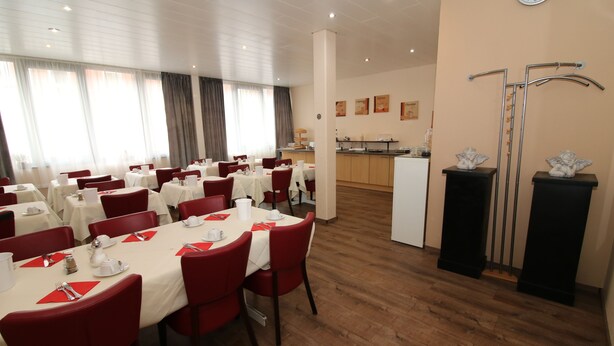 Comedor de hotel con varias mesas dispuestas para comer, una cocina al fondo y una recepción.