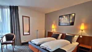A hotel room with a double bed, two bedside lamps, a chair, a large mirror, and a painting on the wall. - Concorde Hotel Ascot (Düsseldorf)